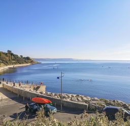 A coastal promenade with people walking and a car with kayaks on the roof near calm water at Lobster Cottage in Brewers Quay Harbour