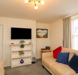 A living room with a mounted television above a white shelf with plants and a vase and a beige sofa with red and blue cushions at Lobster Cottage in Brewers Quay Harbour