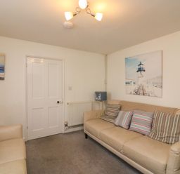 A sitting room with two beige sofas cushions paintings on walls a blue lamp radiator and a door at Lobster Cottage Brewers Quay Harbour