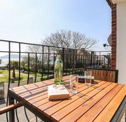 A balcony with a wooden table holding bottles, glasses, and books overlooking a garden and sea at Lookout in Cove Castle