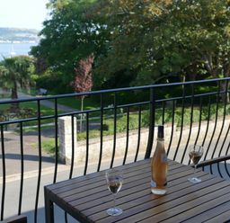 A balcony with a wooden table holding a bottle and two glasses overlooking a garden and water at Lookout in Cove Castle