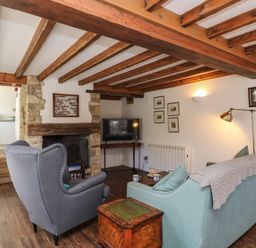 A living room with wooden beams a fireplace a blue sofa and a grey armchair at Lychgate Cottage in Osmington
