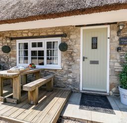 An outdoor wooden table with benches and a tea set in front of a stone cottage with a light green door at Magnolia Cottage Osmington