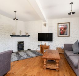 A living room with a wooden coffee table grey sofas a wall-mounted TV and a fireplace at Magnolia Cottage Osmington