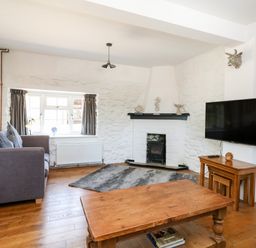 A living room with a gray sofa wooden coffee tables a wall-mounted tv a fireplace and a window with gray curtains at Magnolia Cottage Osmington