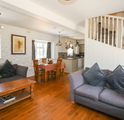 A living room and dining area with sofas, a wooden coffee table, dining table with chairs and kitchen in the background at Magnolia Cottage Osmington