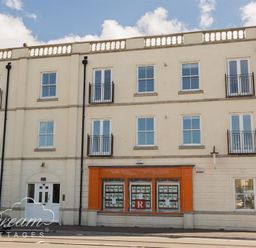 A three-story building with white walls and multiple windows and an orange framed shop window at Marina Vista in Weymouth