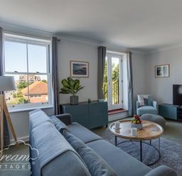 A living room with a blue sofa a round wooden coffee table a floor lamp a blue cabinet a television and windows with gray curtains at Marina Vista in Weymouth