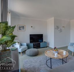 A living room with two blue armchairs a grey pouf a wooden coffee table a television and a plant at Marina Vista in Weymouth