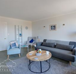 A living room with gray sofa blue armchairs round wooden coffee table and white shelving unit at Marina Vista in Weymouth