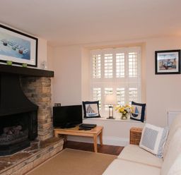 A living room with a stone fireplace a TV on a wooden table cushions on a sofa and a window with shutters at Courtyard House in Dartmouth