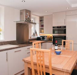 A kitchen with wooden dining table and chairs a bottle of wine and glasses on the table at Courtyard House in Dartmouth