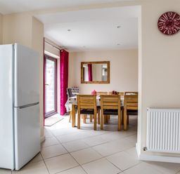 A dining area with wooden chairs around a table a white refrigerator a red clock on the wall and a radiator at New Boathouse Weymouth