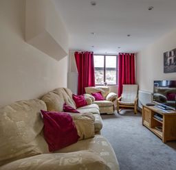 A living room with beige sofas red cushions and curtains a window a TV on a wooden stand and a chair at New Boathouse in Weymouth
