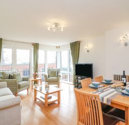 A living room with armchairs a dining table with tableware and a television at Newton's Cove View in Weymouth