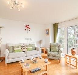 A living room with sofa armchairs coffee table and large glass doors at Newton's Cove View in Weymouth