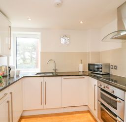 A kitchen with white cabinets black countertops a window a sink a microwave an oven and a stovetop at Newton's Cove View in Weymouth