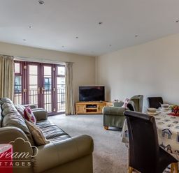 A living room with leather sofas a dining table set with bowls and fruit a television on a wooden stand and double doors with curtains at Old Boathouse in Weymouth