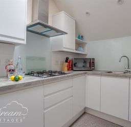 A kitchen with a gas stove, microwave, sink, and white cabinets at Old Boathouse in Weymouth
