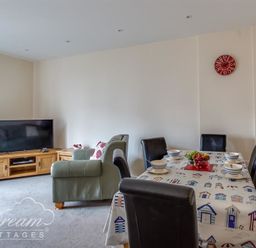 A living room with a TV on a wooden stand a green armchair a dining table with chairs and tableware at Old Boathouse Weymouth