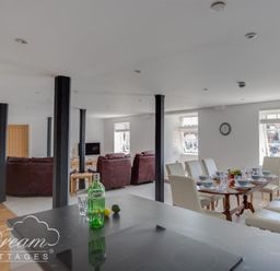A dining area with a table set for eight and a living room with sofas and a TV at Old Coastguard Apartment 2 in Weymouth