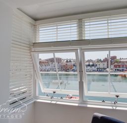 A window with white blinds overlooking a waterfront with buildings at Old Coastguard Apartment 2 in Weymouth