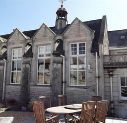 An outdoor patio with wooden chairs and a round table in front of a stone building with large windows and a tower at The Old Portland Courthouse in Portland