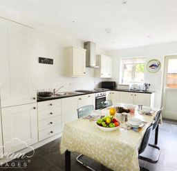 A kitchen with white cabinets black countertops a dining table with a yellow tablecloth and fruit bowl at Olympic Cottage in Portland