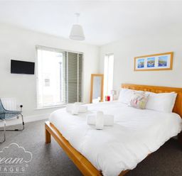 A bedroom with a wooden bed frame and white bedding a chair a wall mounted tv and a framed picture above bed at Olympic Cottage in Portland