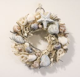 A decorative wreath made of shells starfish and twigs hanging on a white wall at Osprey House Portland in Portland