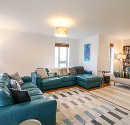 A living room with teal leather sofas a patterned rug two floor lamps and a bookshelf at Osprey House Portland