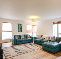 A living room with teal sofas a patterned rug a floor lamp and windows with blinds at Osprey House Portland