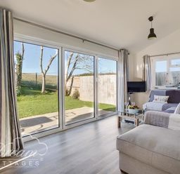A living room with a sofa a glass coffee table a small TV and large sliding glass doors overlooking a garden at Outlook Lodge in Bowleaze