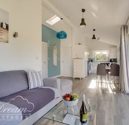 An open living room and kitchen with a sofa glass coffee table dining table and large sliding glass doors at Outlook Lodge in Bowleaze