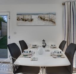 A dining table set for four with black chairs in a room with glass doors and curtains at Outlook Lodge in Bowleaze