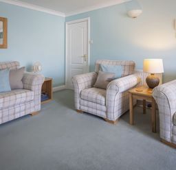 A living room with three plaid armchairs a wooden side table with a lamp a wall mirror and a door at Bakers Dozen 13 Dartmouth House in Dartmouth