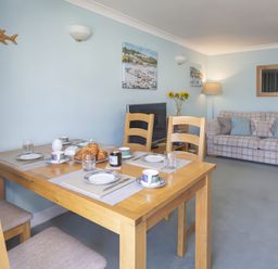 A dining table set with plates cups and croissants in a living room with a sofa and a television at Bakers Dozen 13 Dartmouth House in Dartmouth