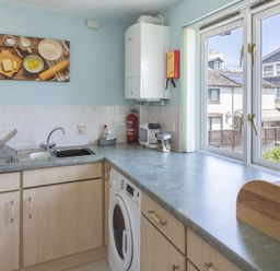 A kitchen with a sink washing machine countertop and window showing houses at Bakers Dozen 13 Dartmouth House in Dartmouth