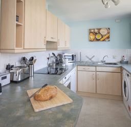A kitchen with wooden cabinets a loaf of bread on a cutting board and various appliances at Bakers Dozen 13 Dartmouth House in Dartmouth