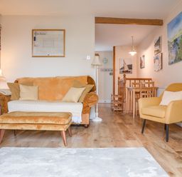 A living room with a sofa, armchair, ottoman, floor lamps, wooden side table, and dining table with chairs at 14a Courtenay Street in Salcombe