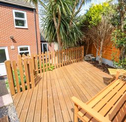 A wooden deck with a bench and small table next to a garden with trees and plants at The Pines in Weymouth