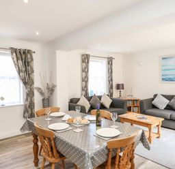 A dining table set with plates and wine bottle beside two sofas with cushions in a living room at The Pines in Weymouth