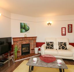 A living room with a white sofa and black flower cushions a red brick fireplace and a TV at Poppies Brewers Quay Harbour