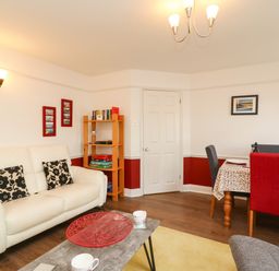 A living room with a white sofa black patterned cushions a wooden bookshelf and a dining table with red and gray chairs at Poppies Brewers Quay Harbour