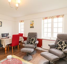 A room with dining table and chairs and two reclining armchairs with cushions at Poppies Brewers Quay Harbour