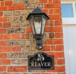 A black outdoor wall lantern above a black nameplate reading Reaver on a red and gray brick wall at Brewers Quay harbour
