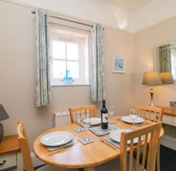 A dining room with a wooden table set for four with plates glasses a blue vase on the window sill and two lamps at Reaver Brewers Quay harbour