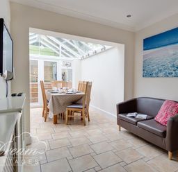 A dining area with a table and chairs next to a brown sofa with a red pillow and a wall-mounted television at Redcliff View Lodge in Weymouth