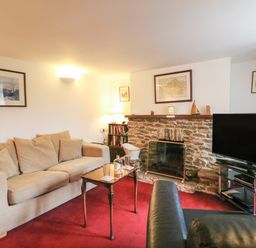 A living room with two sofas a wooden table a stone fireplace and a television at River Cottage in Burton Bradstock