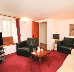A living room with black leather chairs a wooden table a television on a stand and red carpet at River Cottage in Burton Bradstock